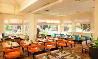 a restaurant with orange and blue chairs , tables , and chairs around the tables , all set for a meal at Hilton Garden Inn Philadelphia/Ft. Washington