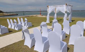 a wedding ceremony set up on a grassy area near a body of water , with white chairs arranged in rows at Mandurah Quay Resort