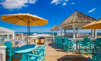 a wooden deck overlooking the ocean , with several chairs and umbrellas placed on the deck for outdoor dining at Ramada Plaza by Wyndham Nags Head Oceanfront