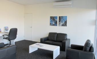 a modern office space with black leather couches , a white coffee table , and two paintings on the wall at Monterey Apartments Moranbah