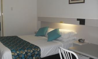 a bed with a floral patterned blanket and two blue pillows is in a room next to a white chair at Balonne River Motor Inn