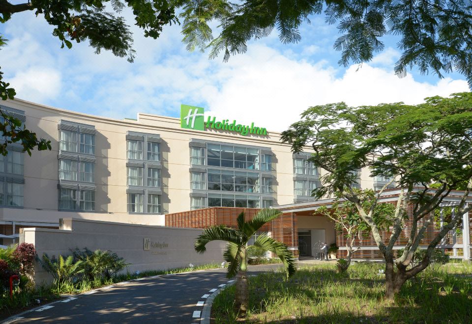 "a large hotel with a green sign that says "" holiday inn "" is surrounded by trees" at Holiday Inn Mauritius Mon Tresor