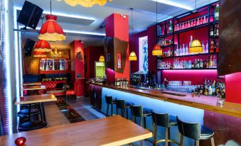 a modern bar with red walls , wooden tables , and chairs , as well as a variety of bottles and glasses at Lux Hotel