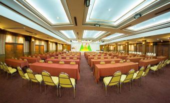 a large conference room with rows of chairs and tables , a stage at the front , and an overhead light fixture at Phrae Nakara Hotel