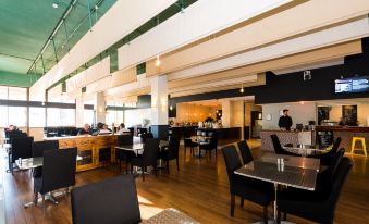 a modern , open - concept restaurant with wooden floors and large windows , featuring black chairs and tables , a bar area , and a bar counter at Greenmount Beach House