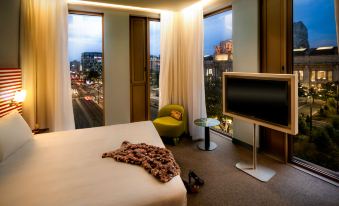a hotel room with a bed , a chair , and a tv , overlooking a cityscape at night at Glam Milano