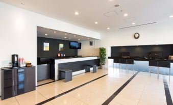 a modern office lobby with a reception desk , white chairs , and a tv mounted on the wall at Dormy Inn Mishima