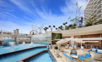 a large swimming pool with a water slide and lounge chairs is surrounded by palm trees at Loisir Hotel Naha