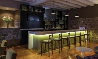 a modern bar with a long wooden counter and stools , along with bottles and wine glasses on display at Novotel Cusco