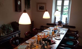 a long dining table set with plates , cups , and utensils in a room with hanging lights at Le Petit Moulin