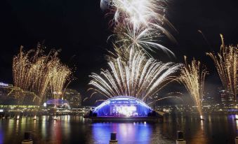 a nighttime scene with fireworks lighting up the sky over a body of water , creating a festive atmosphere at Novotel Sydney Darling Harbour