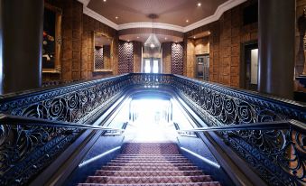 a grand staircase with ornate iron railings leads up to a door at the top at Malmaison Dundee