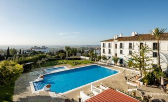 a large swimming pool is surrounded by white buildings and overlooks a city with palm trees at Ilunion Hacienda de Mijas