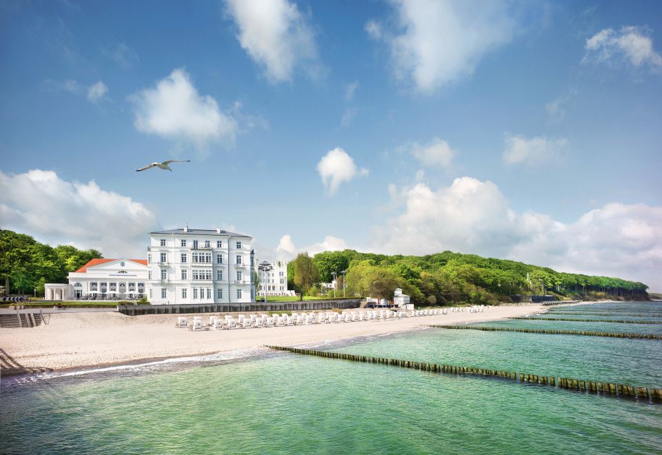 a large white building situated on the beach , with a beautiful blue sky overhead and clear water surrounding it at Grand Hotel Heiligendamm - the Leading Hotels of the World