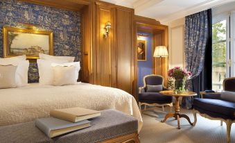 a luxurious bedroom with a large bed , a chair , and a book on the bedside table at Auberge du Jeu de Paume