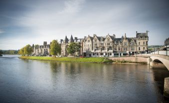 a row of buildings is located next to a body of water , with trees in the background at Columba Hotel Inverness by Compass Hospitality