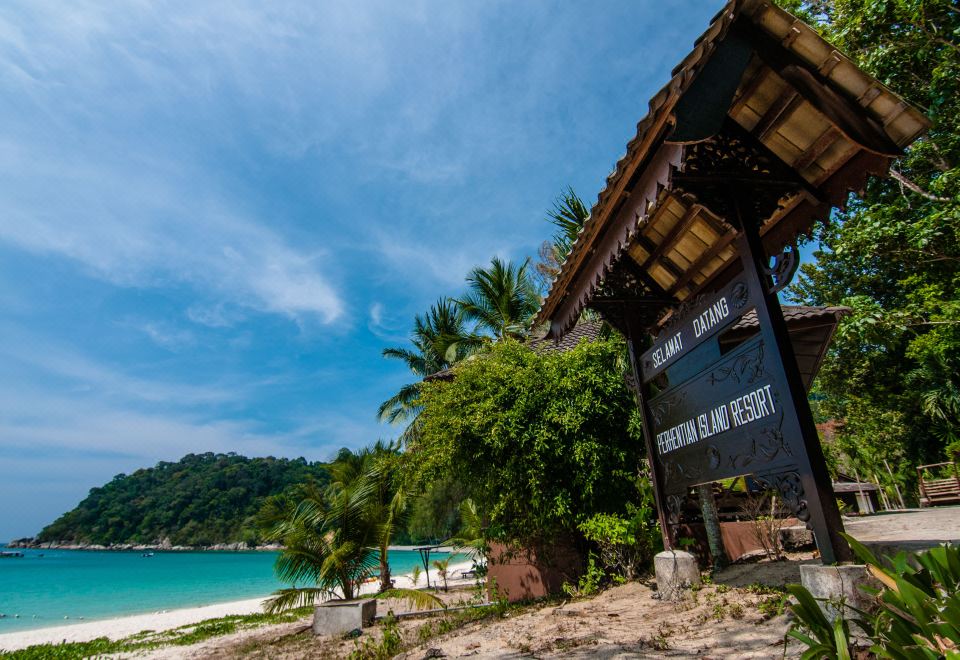 a tropical beach scene with a hut on the shore , surrounded by lush greenery and clear blue water at Perhentian Island Resort