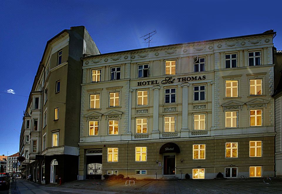 "a large building with a yellow facade and the words "" hotel thomas "" on it is lit up at night" at Hotel Sct. Thomas
