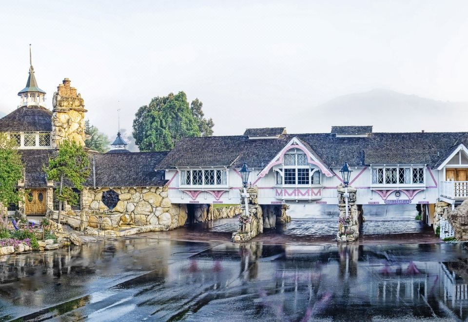 a quaint , stone bridge with a large house and water reflecting its design , surrounded by lush greenery at Madonna Inn