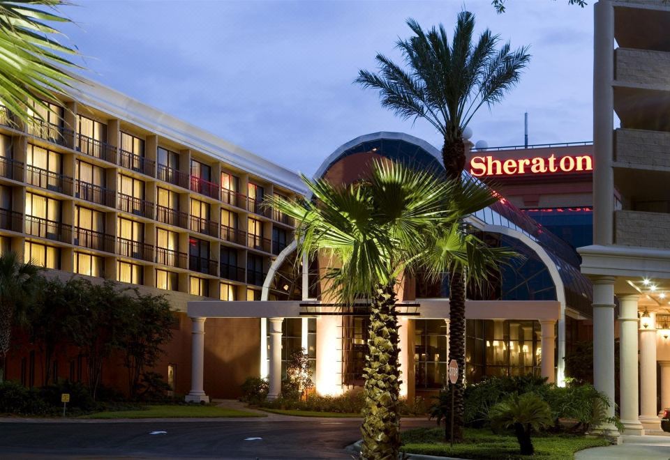 "a large hotel with palm trees in front of it , illuminated at night , and the hotel name "" sheraton "" visible above the entrance" at Sheraton Orlando North Hotel