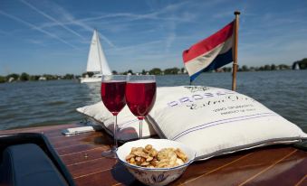 two glasses of wine and a bowl of food are placed on a wooden deck overlooking the water at Fletcher Hotel Restaurant Loosdrecht-Amsterdam