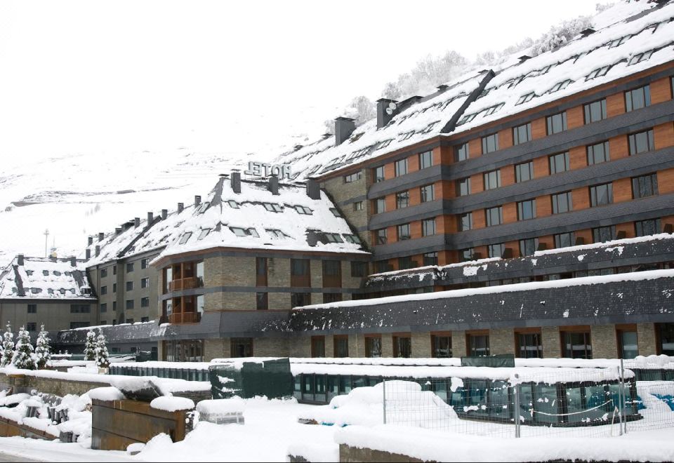a snow - covered building with a large building on the left side and smaller buildings on the right side at Hotel Val de Neu G.L.