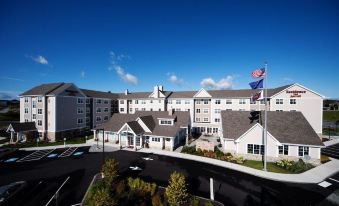 a large , white building with multiple flags flying , surrounded by a parking lot and trees at Residence Inn Auburn