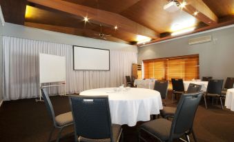 a conference room with a white table surrounded by chairs and a projector screen on the wall at Dog Rock Motel