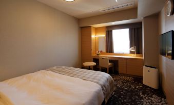 a neatly made bed is in a room with a window and a desk , next to it is a desk with a lamp at Hotel Monte Hermana Fukuoka