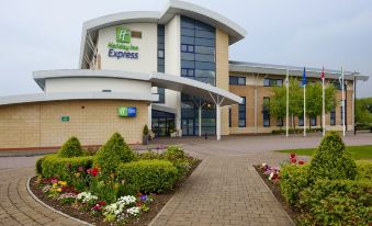 "a large building with a sign that says "" holiday inn express "" is surrounded by flowers and bushes" at Holiday Inn Express Northampton - South