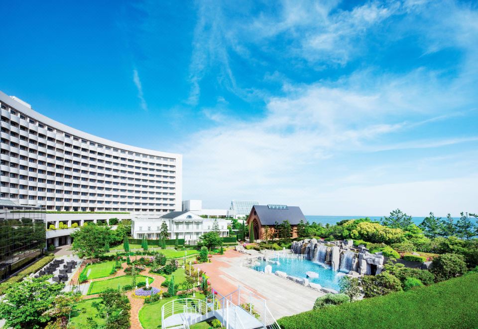 a large white building with a pool in front of it , surrounded by trees and grass at Sheraton Grande Tokyo Bay Hotel