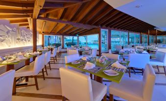 a modern restaurant with white chairs and tables , green tablecloths , and large windows overlooking the ocean at Hotel Dann Cartagena