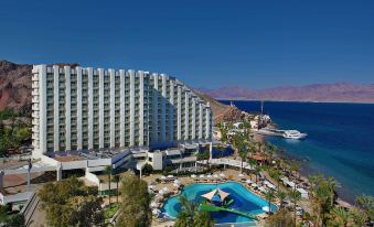 a large hotel with a pool and palm trees in front of it , surrounded by mountains at Steigenberger Hotel & Nelson Village, Taba
