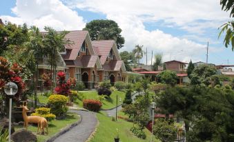 a house is surrounded by a lush green garden with flowers and trees , while a cow grazes on the grass at Khas Parapat