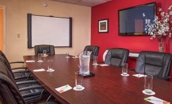 a conference room with a large wooden table , black chairs , and a television mounted on the wall at Courtyard Hampton Coliseum Central