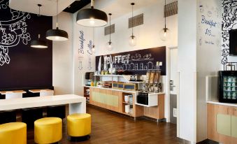 a modern coffee shop with white walls , wooden floors , and yellow stools around a counter at Ibis Budget Auckland Airport