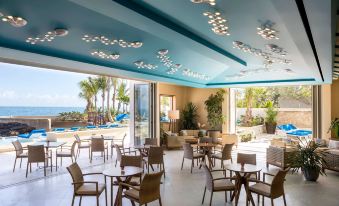 a modern restaurant with multiple tables and chairs , surrounded by palm trees and the ocean at Condado Vanderbilt Hotel