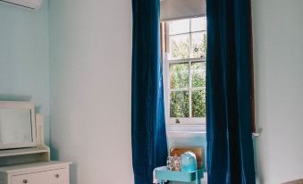 a cozy bedroom with blue curtains , white walls , and a window with curtains drawn on it at Terroir Auburn