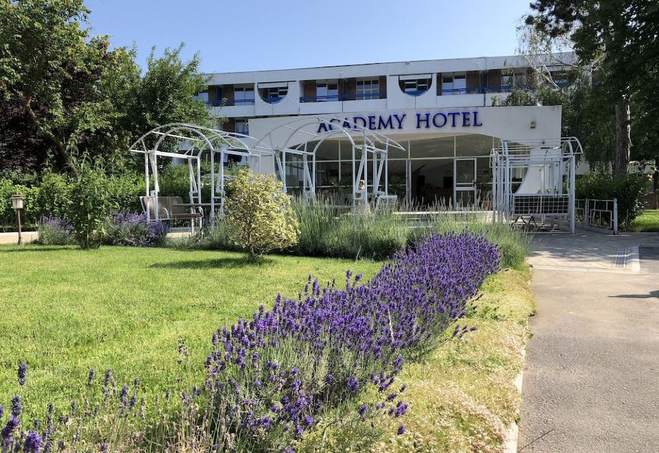 the exterior of the academy hotel , a white building with a blue sign and lush greenery surrounding it at Academy Hotel