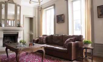 a cozy living room with a brown leather couch , a wooden coffee table , and a red rug at Joie de Vivre