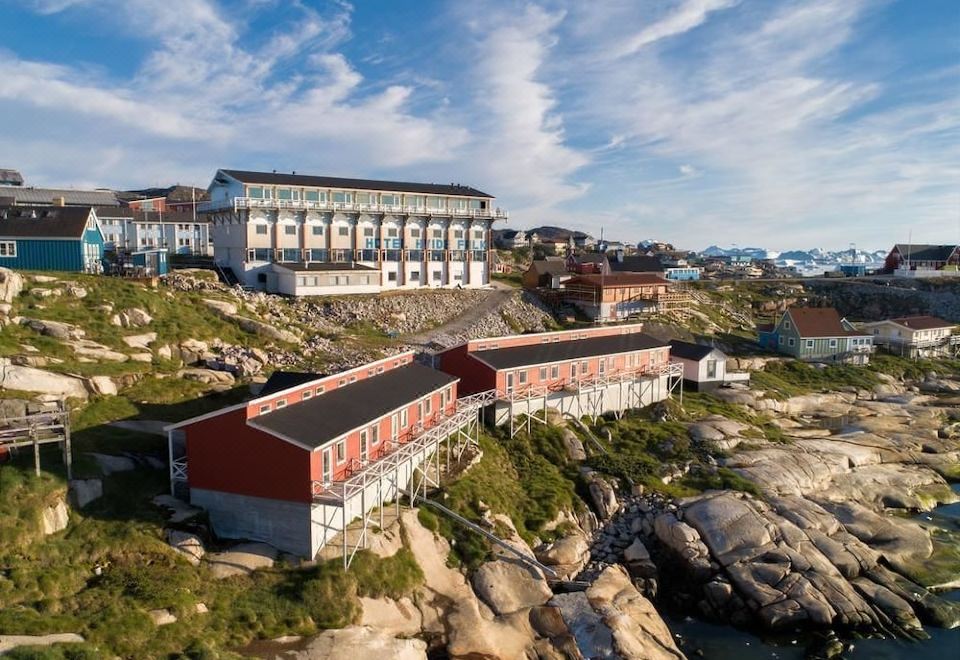 a large white building with red and black accents is perched on a rocky cliff at Hotel Hvide Falk