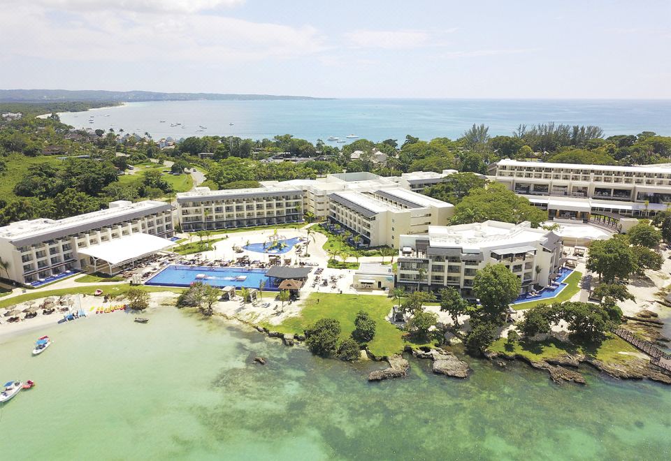 an aerial view of a resort with a large building and swimming pool surrounded by trees and water at Royalton Negril, An Autograph Collection All-Inclusive Resort
