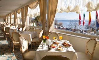 a dining room with a table set for breakfast , surrounded by chairs and a window overlooking the ocean at Corfu Palace Hotel