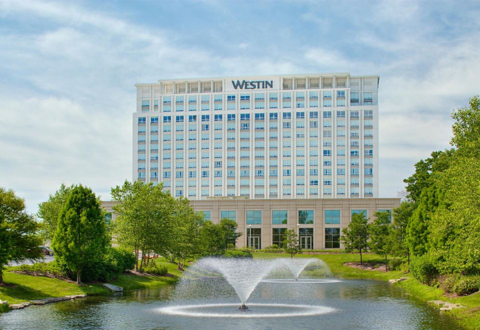 a large white hotel with a water fountain in front of it , surrounded by trees and grass at The Westin Chicago North Shore