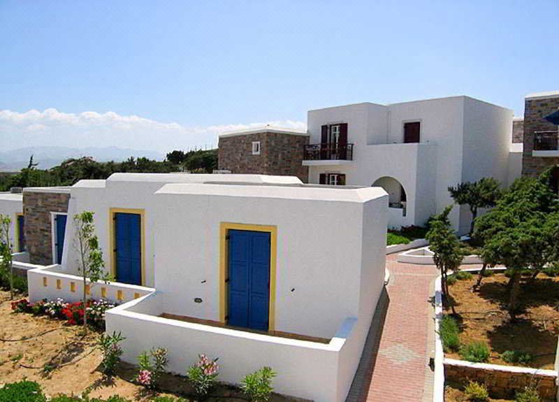 a white building with blue doors and windows , surrounded by green grass and trees , under a clear sky at Naxos Palace Hotel