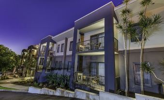 a modern apartment building with multiple balconies and a well - lit exterior at night , surrounded by trees and palm trees at Quest Ipswich