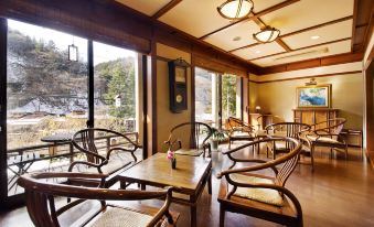 a cozy coffee shop with wooden furniture , including chairs and tables , situated in front of a large window at Shima Onsen Kashiwaya Ryokan
