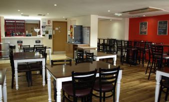 a large dining room with several tables and chairs , a kitchen in the background , and a red wall at 247Hotel.Com