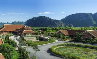 a beautiful landscape with mountains in the background , a road winding through a park , and various buildings at Emeralda Resort Ninh Binh