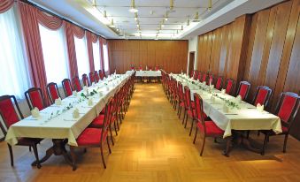 a long dining table with white tablecloths and red chairs is set up in a large room at Hotel Alexandra